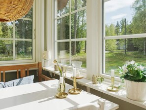 A room with a large window, a white table, and a wicker chair. - 4 Star Holiday Home in Grisslehamn (Grisslehamn)