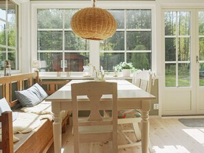 A dining area with a wooden table and chairs, a bench with cushions, and a hanging light fixture. - 4 Star Holiday Home in Grisslehamn (Grisslehamn)