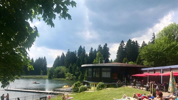 Ein Außenbereich am See mit Pool, Liegestühlen und einem Gebäude mit gewölbtem Dach.