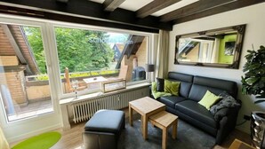 Ein modernes Wohnzimmer mit einem schwarzen Ledersofa, einem Holztisch und einem großen Fenster mit Blick auf eine grüne Landschaft.