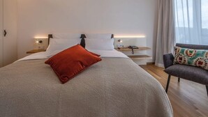 A modern hotel room with a large bed, bedside tables with lamps, a chair, and a window with sheer curtains. - Suite Apartment 80 sqm (Gaienhofen)