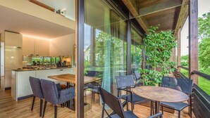 A modern kitchen with a central island, a dining area with a round table and chairs, and a view of greenery through large glass doors. - Suite Apartment 80 sqm (Gaienhofen)