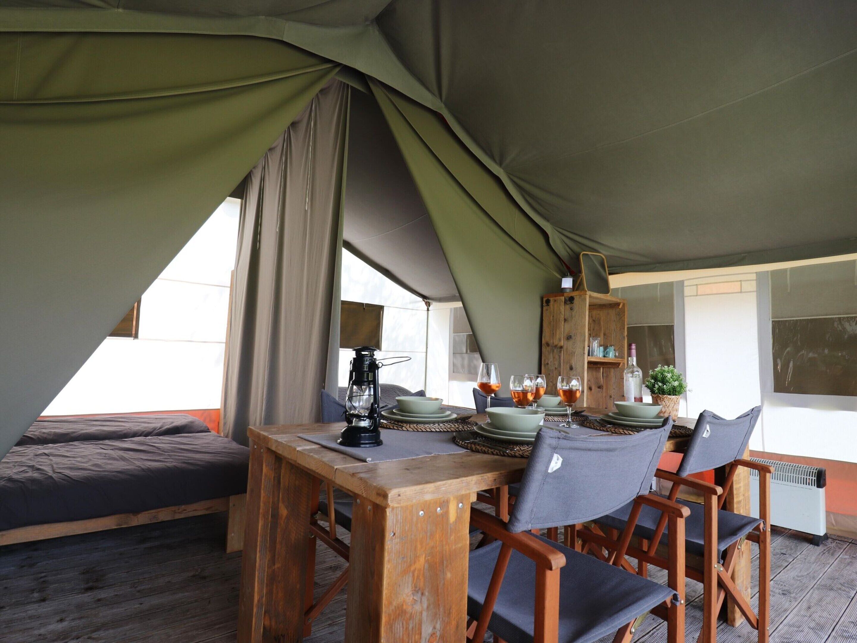 A tented dining area with a table set for four, a lantern, and a wooden cabinet with dishes.