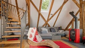 A loft-style room with exposed wooden beams, a staircase, a sofa set, a red rug, and a wood-burning stove. - Zum Kuckuck Black Forest (Schonach im Schwarzwald)