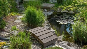 A garden with a pond, a wooden bench, and a stone pathway. - Zum Kuckuck Black Forest (Schonach im Schwarzwald)