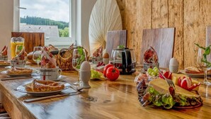 A breakfast table with various foods and drinks, a view of the outdoors, and a rustic wooden wall. - Zum Kuckuck Black Forest (Schonach im Schwarzwald)