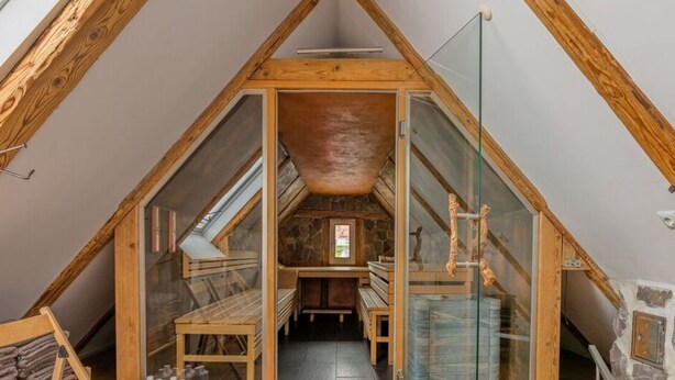 A triangular attic room with a sloped ceiling, wooden beams, a stone wall, and a small window. - Zum Kuckuck Black Forest (Schonach im Schwarzwald)