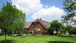 Una grande casa in mattoni con tetto spiovente, circondata da un prato curato e alberi.
