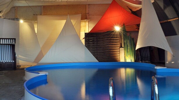 Una piscina interna con rivestimento blu, circondata da tende bianche e rosse.