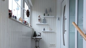 Ein schmaler Flur mit weißen Wandverkleidungen, einem kleinen Tisch mit einem Weihnachtsbaum und Rentieren sowie Regalen mit Weihnachtsdekoration.