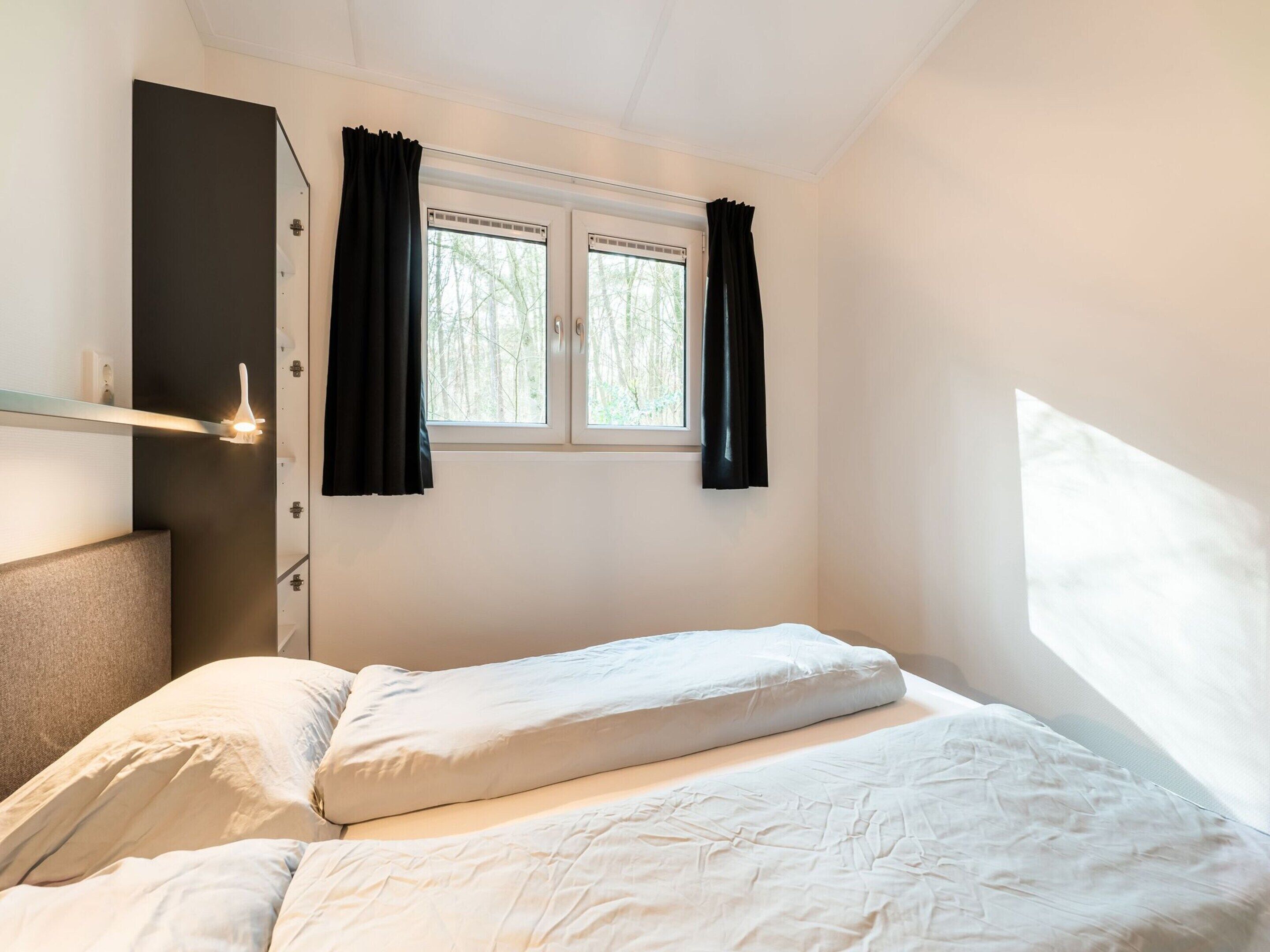 A bedroom with a bed, a window with curtains, and a shelf with a light fixture.