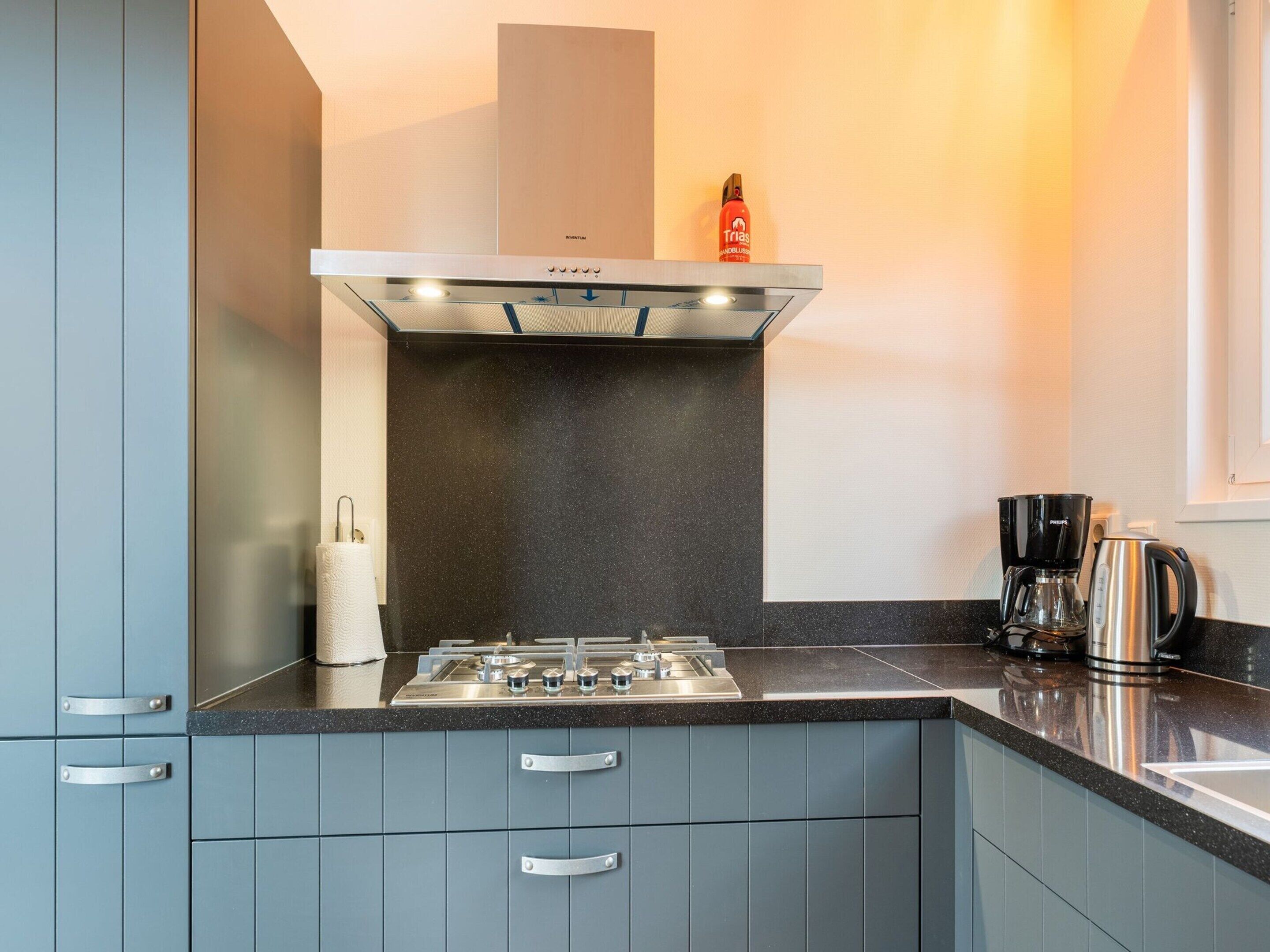 A modern kitchen with grey cabinets, a stainless steel range hood, and a coffee maker on the counter.