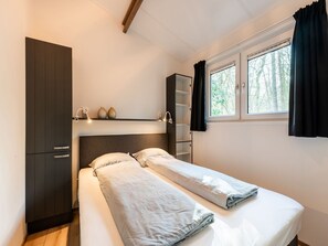 A bedroom with a bed, a wardrobe, a shelf with decorative items, and a window with curtains.