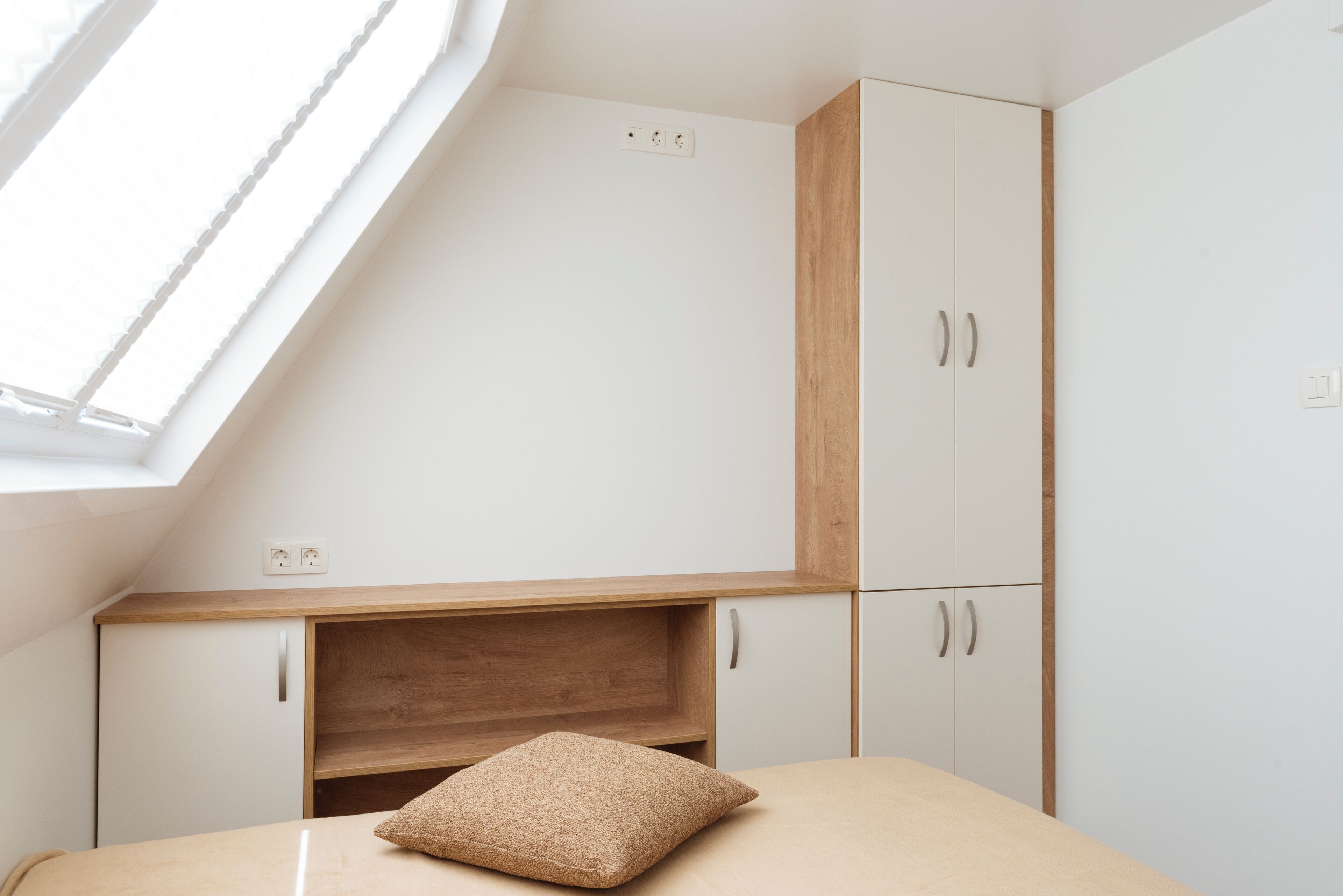 A bedroom with a skylight, a bed with a textured pillow, and a wooden headboard.