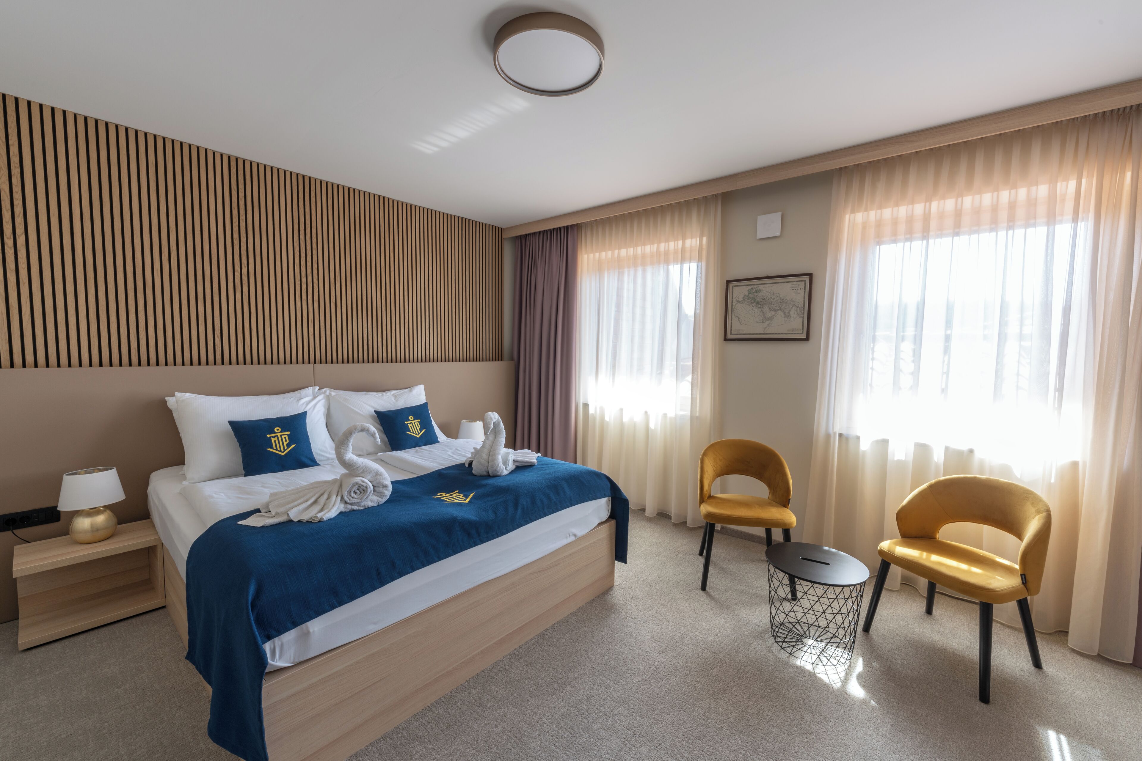 Una habitación de hotel con una cama, dos sillas, una mesita y una mesita de noche con lámpara.