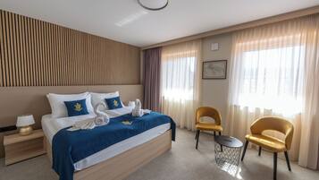 Una habitación de hotel con una cama, dos sillas, una mesita y una mesita de noche con lámpara.