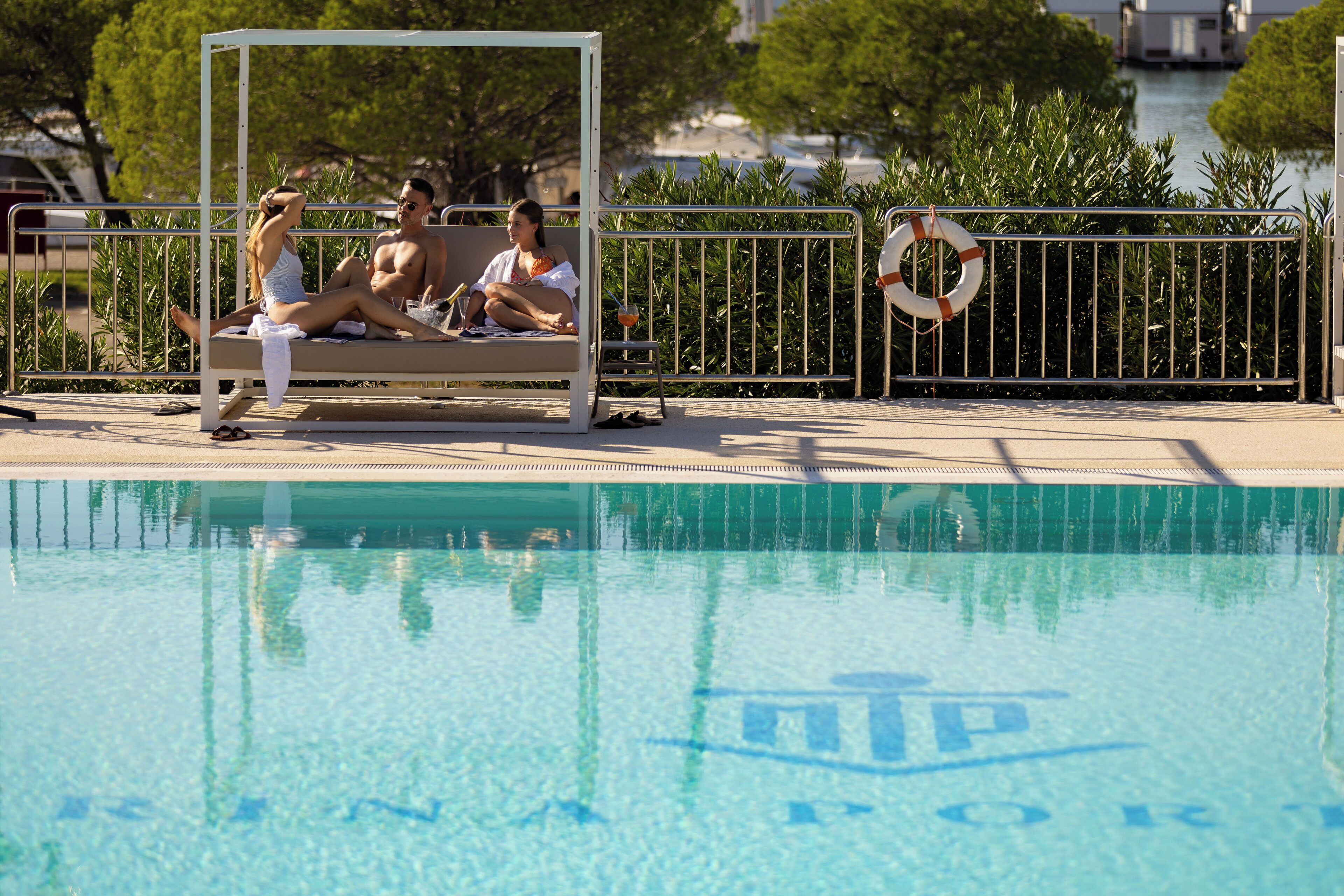 A pool area with a lifebuoy on the railing, a covered seating area, and a clear view of the water.