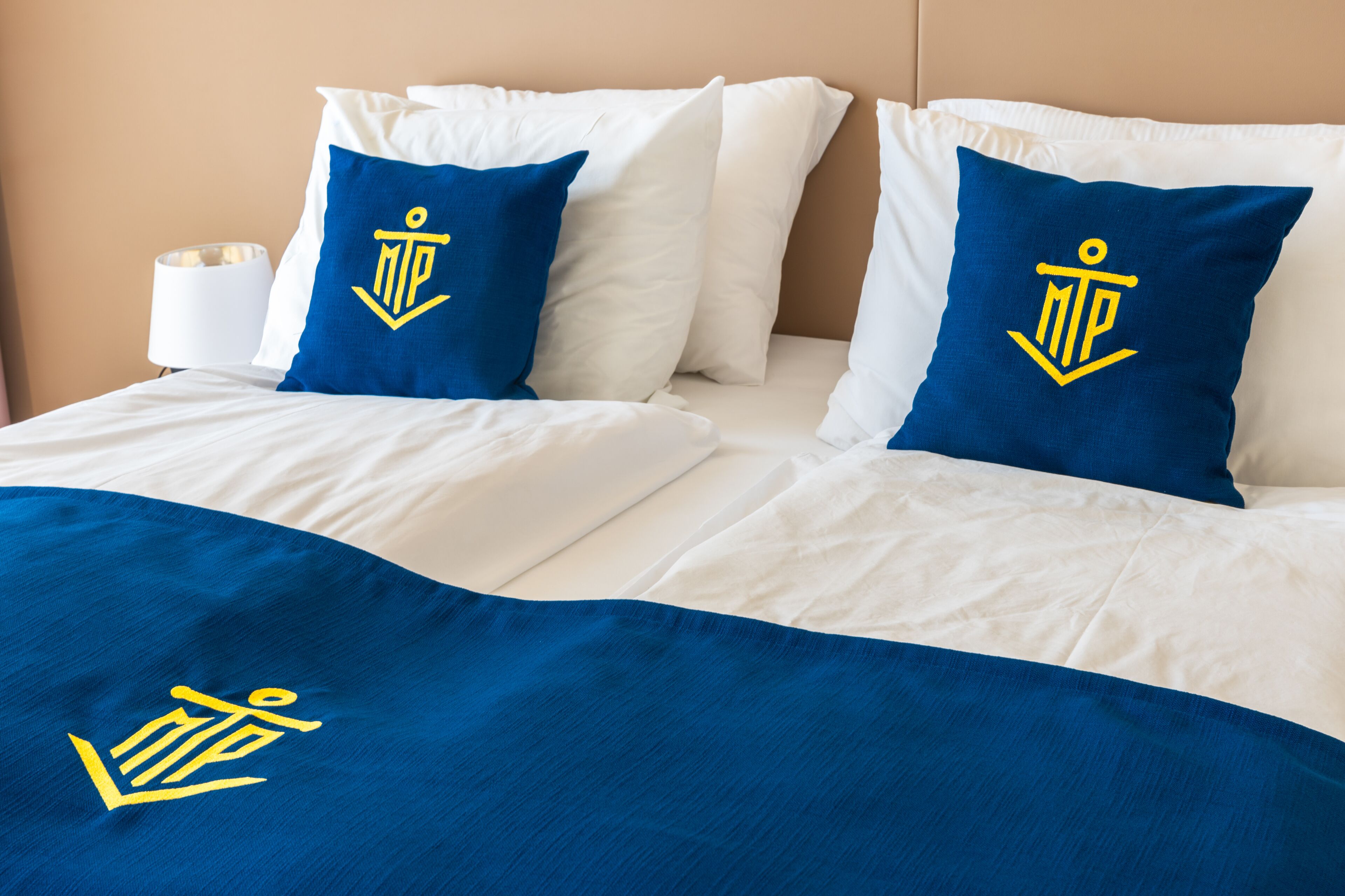 A neatly made bed with white bedding and two blue pillows featuring a yellow anchor logo.