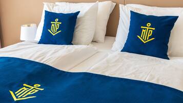 A neatly made bed with white bedding and two blue pillows featuring a yellow anchor logo.