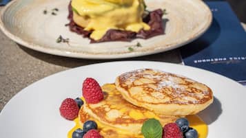 Two plates of food, one with pancakes and berries and the other with a dessert.