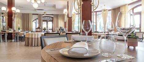 A dining area with round tables, chairs, and a variety of table settings including plates, glasses, and cutlery.