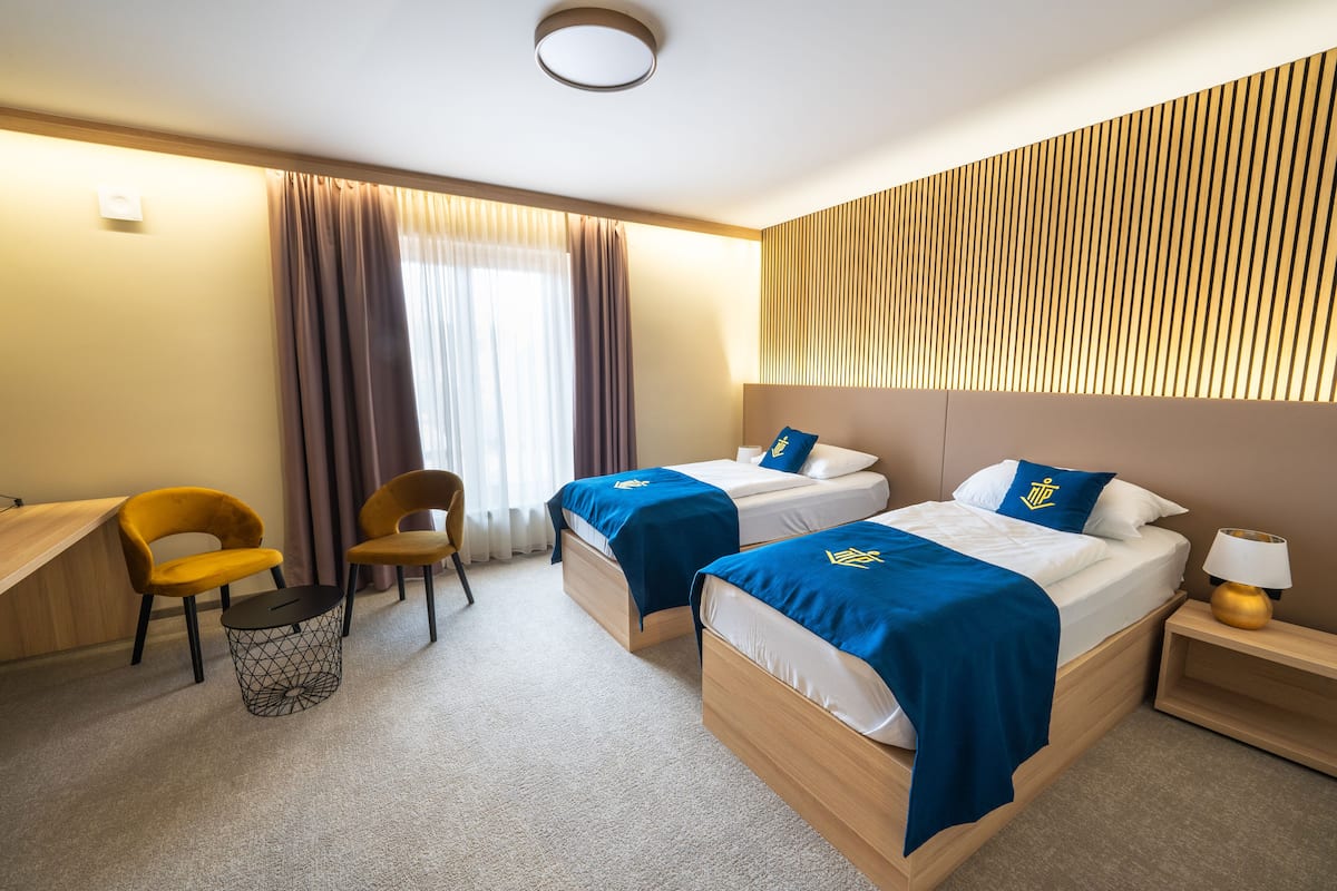 Una habitación de hotel con dos camas, un escritorio, una silla y una lámpara.