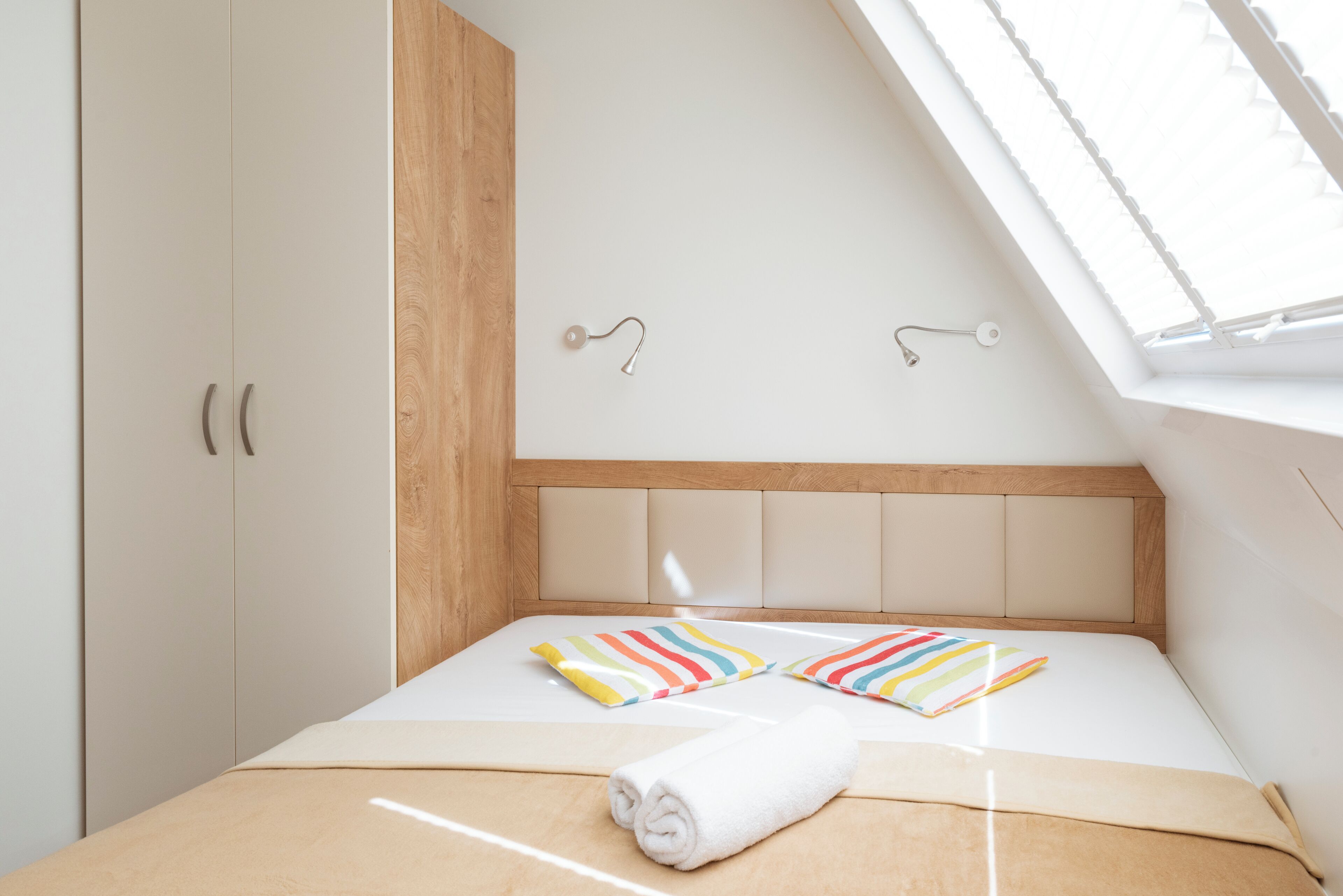 Un dormitorio con techo inclinado, una cama con almohadas a rayas, una toalla enrollada y un cabecero de madera.