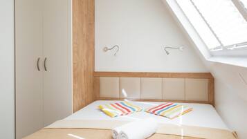 Un dormitorio con techo inclinado, una cama con almohadas a rayas, una toalla enrollada y un cabecero de madera.