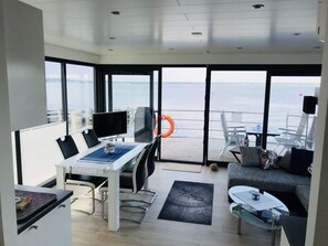 En moderne stue med et stort vindue med havudsigt, et spiseområde med bord og stole, og en hyggelig siddekrog med sofa og sofabord.