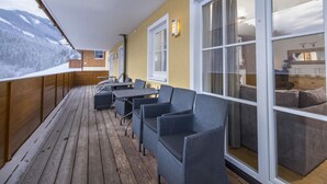 Ein überdachter Außenbereich mit Holzboden und grau gepolsterten Stühlen.