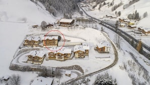 Ein verschneites Dorf mit traditionellen Chalets, einer kurvigen Straße und einem Berg im Hintergrund.