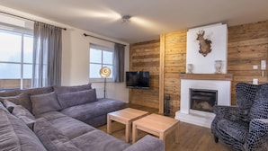 Ein Wohnzimmer mit einer Couch, einem gemusterten Sessel, einem Kamin und einem an der Wand befestigten Fernseher.