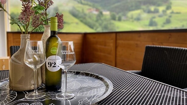 Ein Tisch mit einer Weinflasche, zwei Weingläsern und einer Vase mit Blumen.