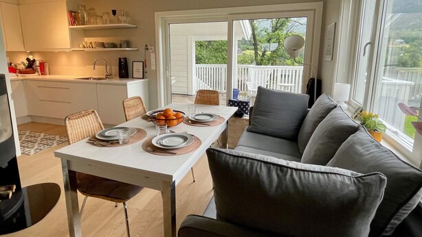 A modern kitchen with white cabinets, a dining table set for four, and a gray sofa. - 6 Person Holiday Home in Bjoa (Vindafjord)