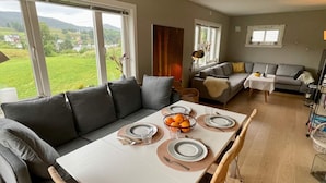A dining area with a table set for four, a grey sofa, and a view of the outdoors. - 6 Person Holiday Home in Bjoa (Vindafjord)