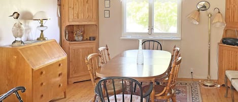 A dining area with a wooden table and chairs, a rug, and a window with curtains.