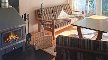 Una sala de estar acogedora con una estufa de leña, un sofá, una mesa y una cesta de mimbre.