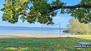 A beach volleyball net with a picnic table nearby, a grassy area with fallen leaves, and a clear view of the water. - 6 Person Holiday Home in Vingaker (Vingåker)