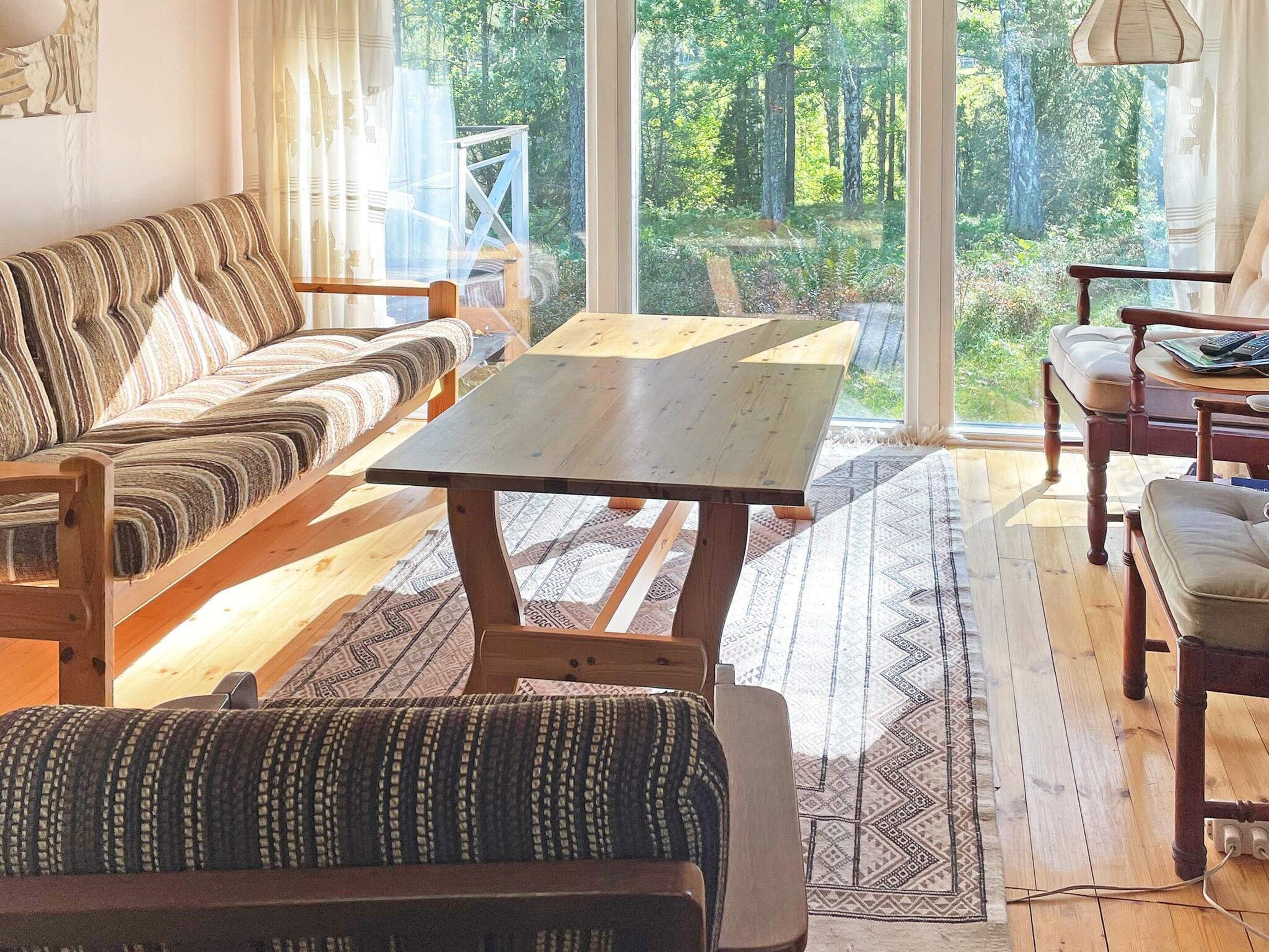 A cozy room with a sofa, a wooden table, and a view of a forest through large windows.