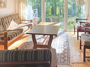 A cozy room with a sofa, a wooden table, and a view of a forest through large windows. - 6 Person Holiday Home in Vingaker (Vingåker)