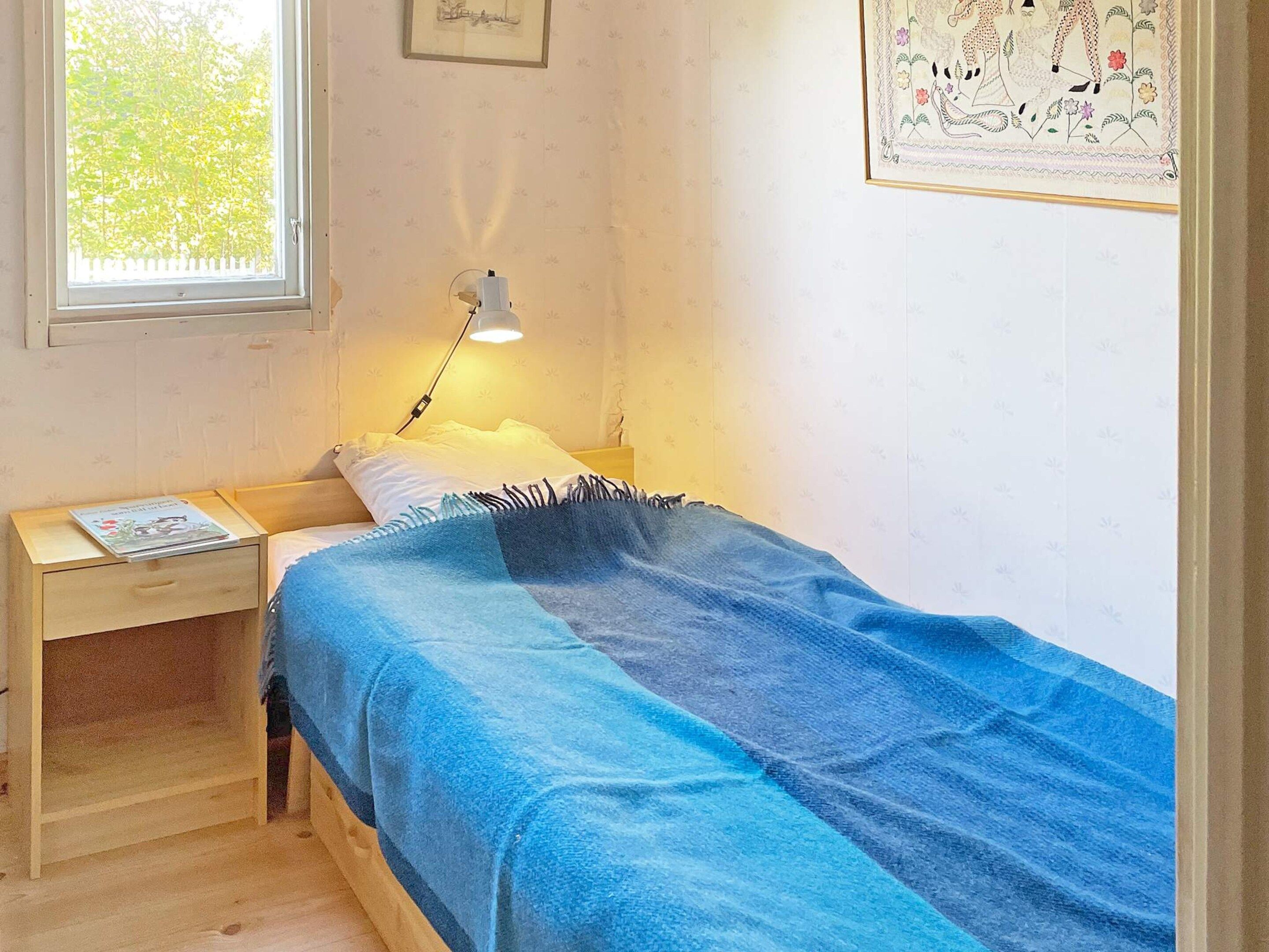 Une chambre avec un lit simple, une table de chevet, une lampe et une fenêtre.