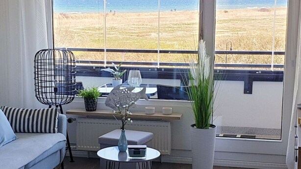 Una habitación con vistas a la playa, un sofá, una mesita con un florero y una planta en maceta.
