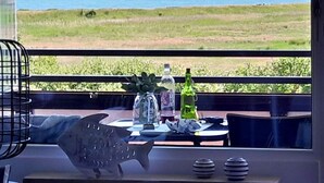 Un balcón con vista al mar, una mesa con decoración de pez, una botella y un florero.