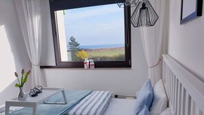 Un dormitorio con cama, mesita de noche, ventana y vista al mar, además de un radiador.