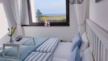 A bedroom with a bed, a bedside table, a window with a view of the sea, and a radiator.