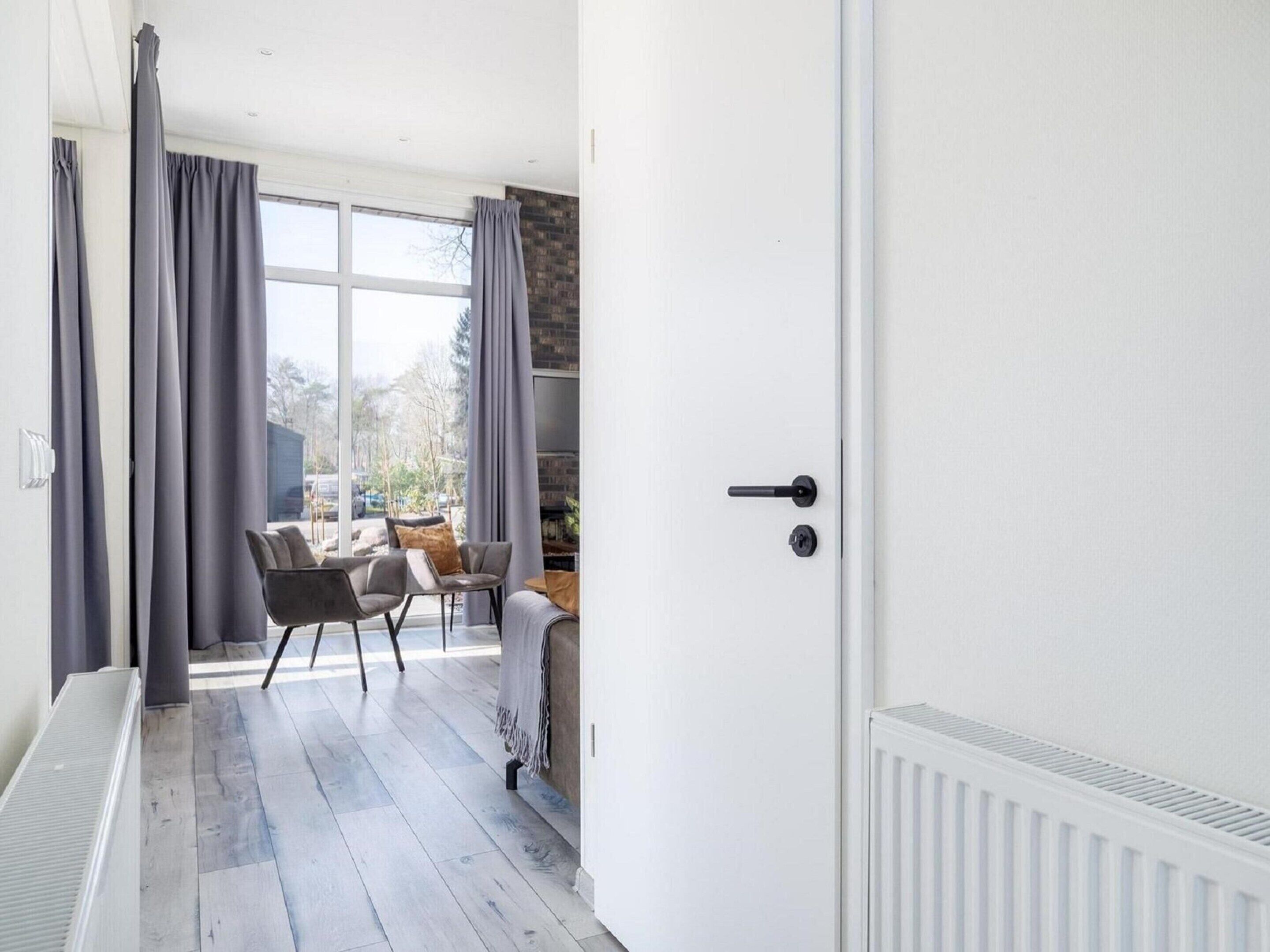 A modern living room with a large window, grey curtains, a white door, and a radiator.