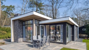 A modern house with a patio area featuring a dining table and chairs. - Luxury Stay Near Veluwe Park (Hoenderloo)
