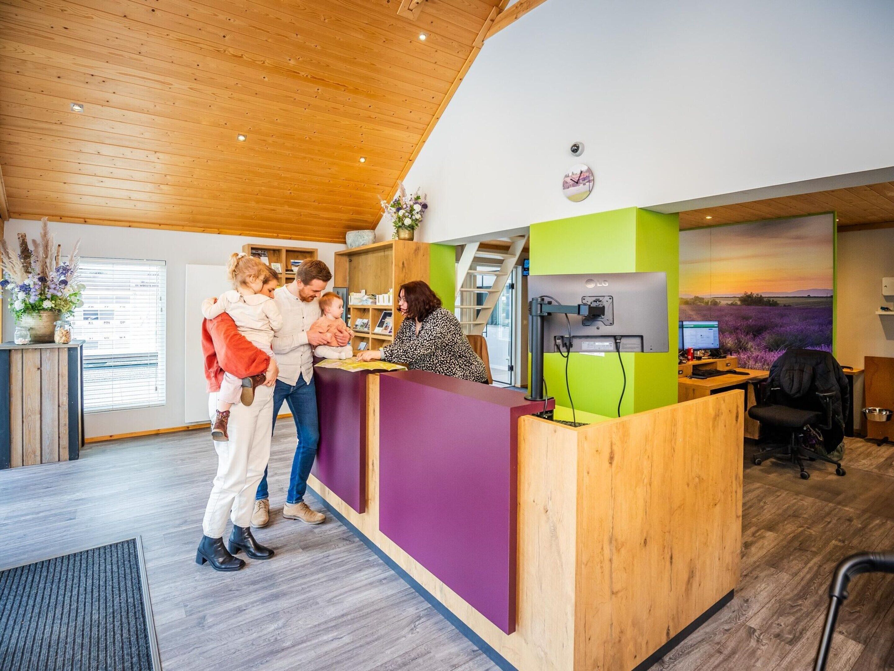 A reception desk with a wooden counter, a green and purple wall, and a computer monitor.