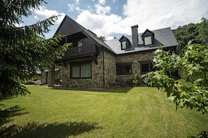 Uma casa de pedra com varanda, chaminé e um gramado bem cuidado.