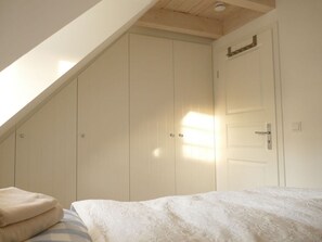 A bedroom with a sloped ceiling, a bed with a white bedspread, and a wardrobe with a light-colored door. - Favorite Place Modern Retreat (Wrixum)